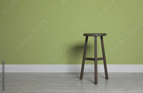 Stylish wooden stool near light green wall indoors. Space for text