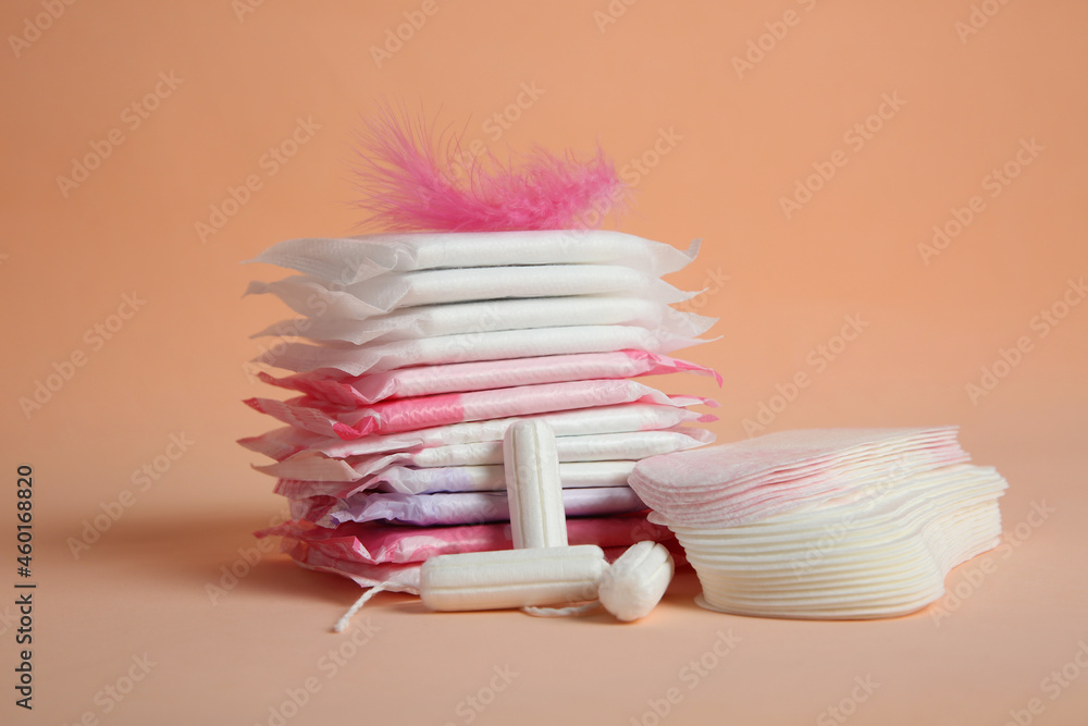Menstrual pads with pink feather and other period products on pale orange background - obrazy, fototapety, plakaty 