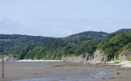 Tree covered cliffs and hills with muddy bay and blue sky
