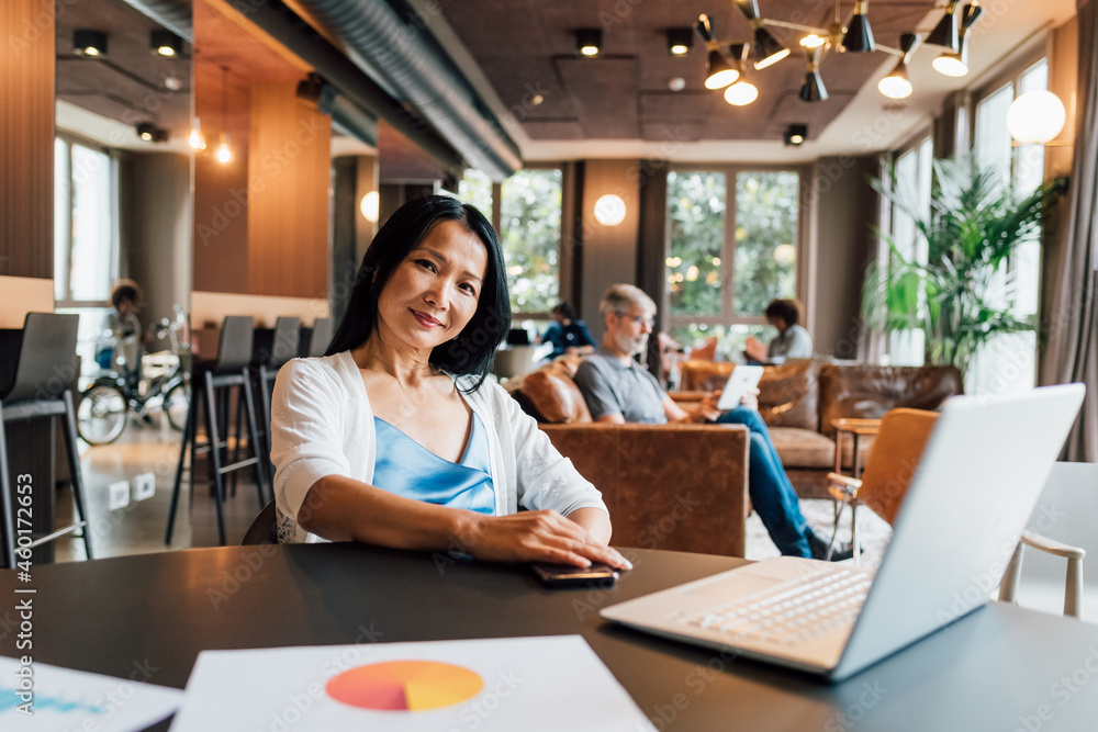 Italy, Portrait of smiling businesswoman at table in creative studio Italy, Portrait of smiling businesswoman at table in creative studio