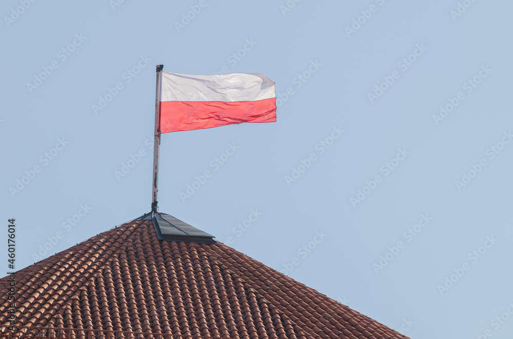 biało czerwona flaga polski zawieszona na wieży z czerwoną dachówką - obrazy, fototapety, plakaty 