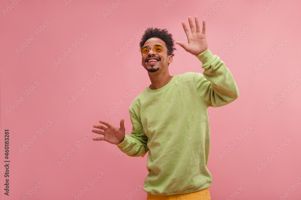 Happy young African guy raising hands up and circling around himself on pink background. Funny model boy in good mood in sunglasses is dressed pistachio jacket. Leisure concept youth, active lifestyle Happy young African guy raising hands up and circling around himself on pink background. Funny model boy in good mood in sunglasses is dressed pistachio jacket. Leisure concept youth, active lifestyle