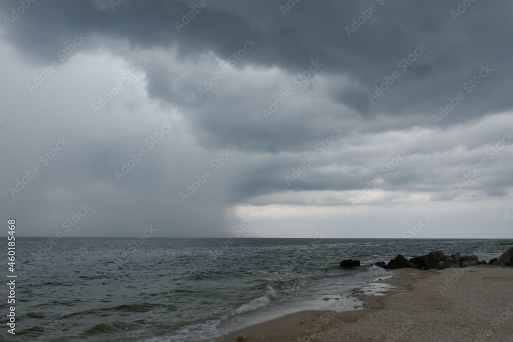 Gloomy beach with black stones and the stormy sea. Dark gray clouds on the coastline over the water.