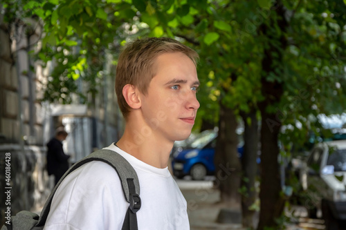 Street portrait of a smiling young guy 20-25 years old with a backpack on his shoulder against the background of old urban architecture. Perhaps he is an IT specialist or a tourist, a student or a nov