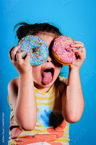 Funny boy on bright blue wall background. Beautiful child is having fun with donut. Yellow, pink and turquoise colors