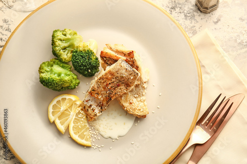 Plate with baked cod fillet, sauce and broccoli on grunge background