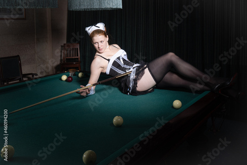Young sexy chambermaid plays billiard. Pin up style. photo