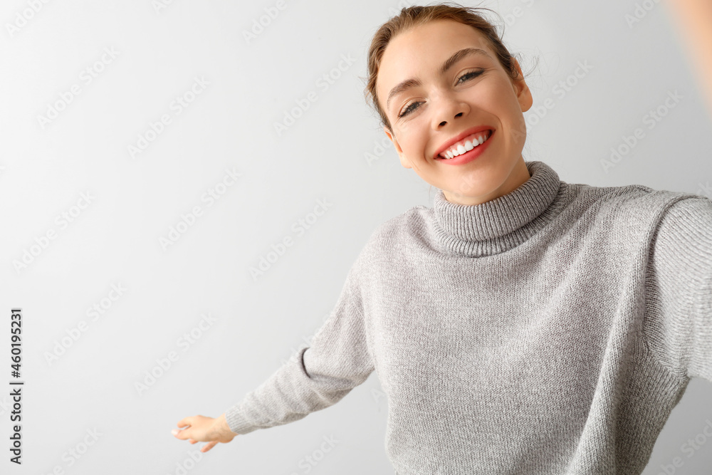 Young woman taking selfie on light background Young woman taking selfie on light background