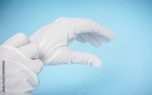 Person putting on surgical gloves. Isolated blue light background. Copy space.