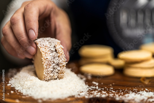 Hand of an unrecognizable person making homemade argentine alfajor spreading it grated coconut photo