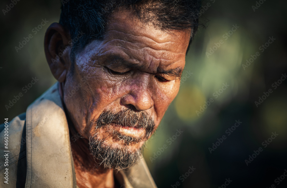 Portrait of Asian old thoughtful man in park with green background, senior depression