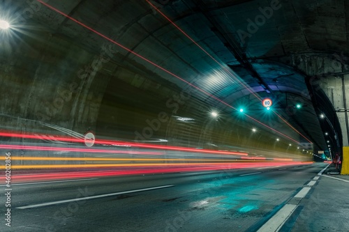 Red and orange trails of car lights passing fast through the highway tunnel in perspective.