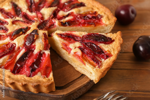 Board with piece of tasty plum pie on wooden background, closeup