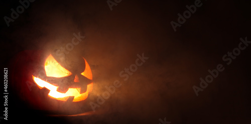Spooky carved Jack o Lantern glowing a fiery red with thick smoke poring out of the face with a scary evil grin.