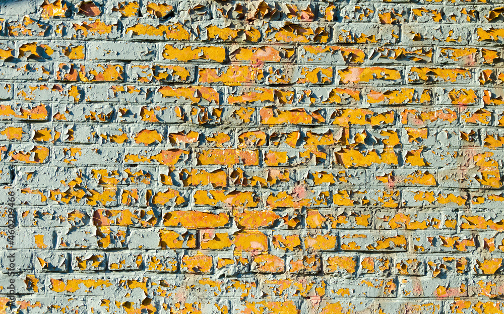 A brick wall made of yellow brick with peeling paint.