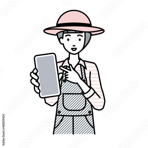 立ってスマートフォンを指差してこちらに向けて見せている農家の女性