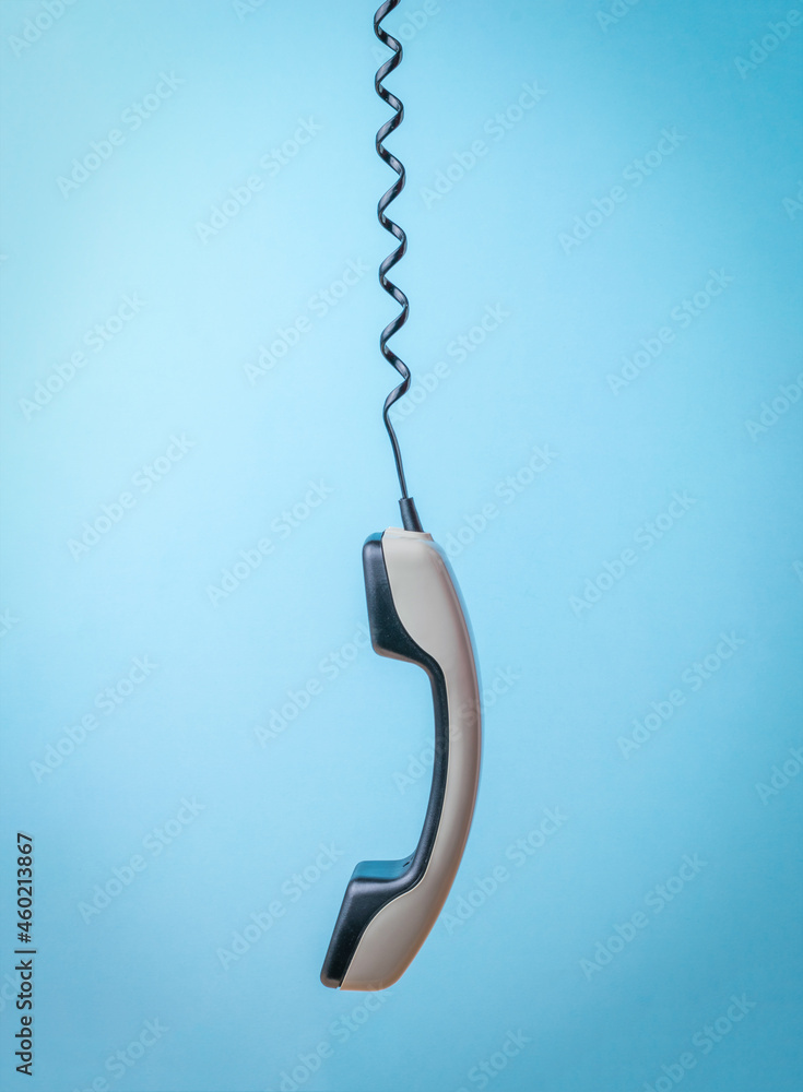 A gray handset on a stretched telephone wire on a blue background. A gray handset on a stretched telephone wire on a blue background.