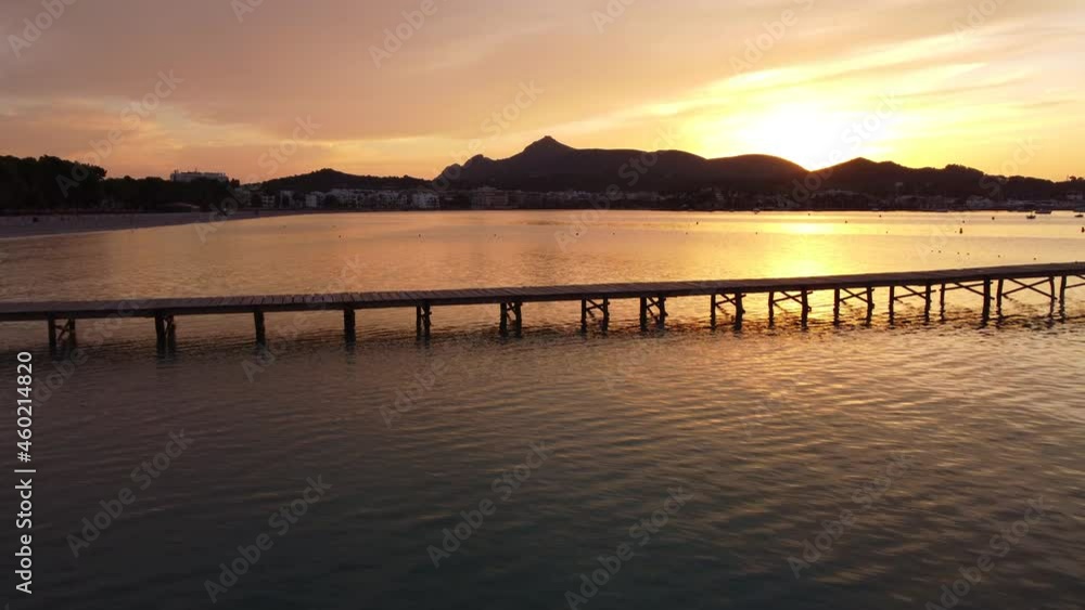 Beautiful Sunrise at Playa de Alcúdia, Mallorca. Drone flying over pier with mountains in background. Popular tourist destination (4K) Beautiful Sunrise at Playa de Alcúdia, Mallorca. Drone flying over pier with mountains in background. Popular tourist destination (4K)