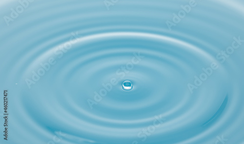 Water drop on water surface with baby blue light effects background.