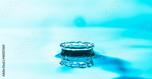 Water drop splashes on the water surface and creates a crown of droplets on colourful of blue background. 