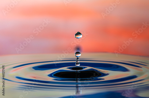 Water droplet splash and make perfect ripples on water surface with orange background.