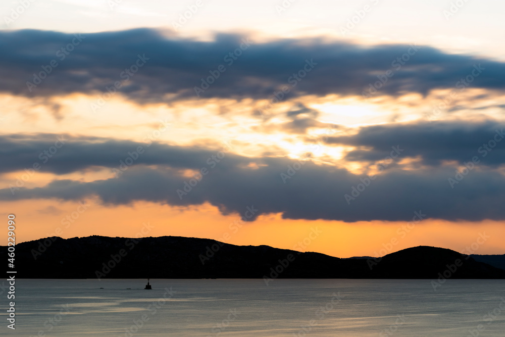 Stunning sunrise over the silhouette of a coastline bathed by a calm sea. Cloudy, dramatic sky, Sardinia, Italy. Stunning sunrise over the silhouette of a coastline bathed by a calm sea. Cloudy, dramatic sky, Sardinia, Italy.