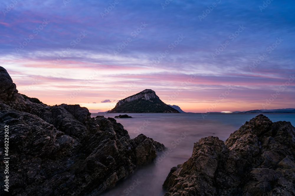 Stunning view of Figarolo island during a romantic and relaxing sunrise with a calm water and some rocks in the foreground. Golfo Aranci, Sardinia, Italy. Stunning view of Figarolo island during a romantic and relaxing sunrise with a calm water and some rocks in the foreground. Golfo Aranci, Sardinia, Italy.