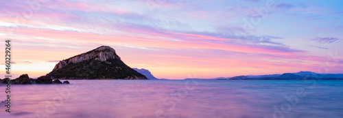 Stunning view of Figarolo island during a romantic and relaxing sunrise reflected on a calm water flowing in the foreground. Golfo Aranci, Sardinia, Italy.