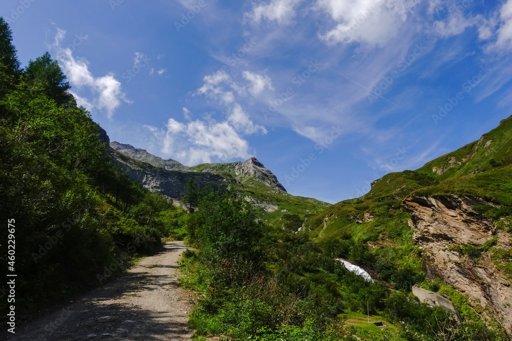 Fototapeta premium dirt road through a green mountain landscape with blue sky