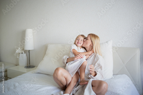 little girl hugging with mom while sitting on the bed in the bedroom