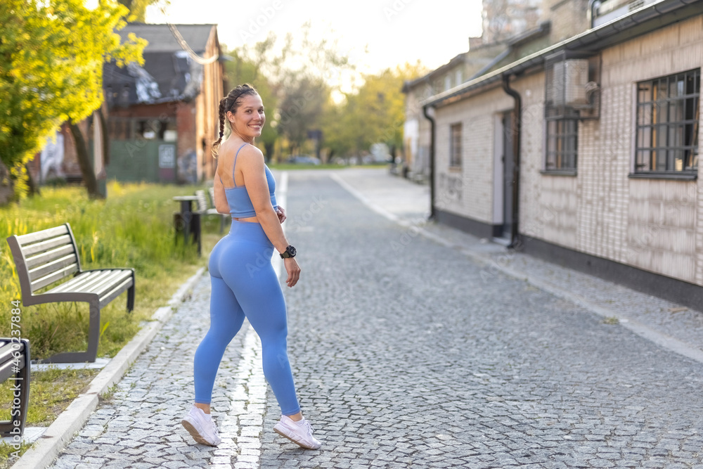 Young fitness female model in blue training sportswear ready for workout on street city valley. Full length backside body view.