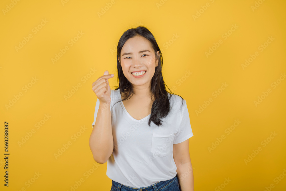 Portrait of young beautiful Asian woman with long dark hair wears white t-shirt showing mini heart gesture isolated on yellow background Portrait of young beautiful Asian woman with long dark hair wears white t-shirt showing mini heart gesture isolated on yellow background