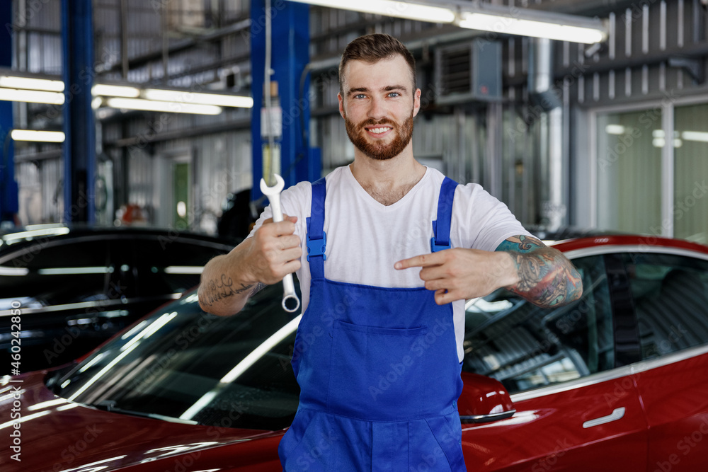 Happy young male professional technician car mechanic repairman man in  denim blue overalls white t-shirt hold point finger on wrench key tool work  in light modern vehicle repair shop workshop indoor Photos