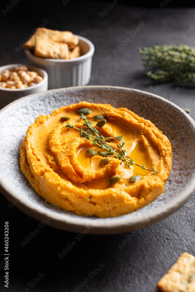 Bowl with pumpkin hummus, delicious appetizer decorated with greens and spices Bowl with pumpkin hummus, delicious appetizer decorated with greens and spices