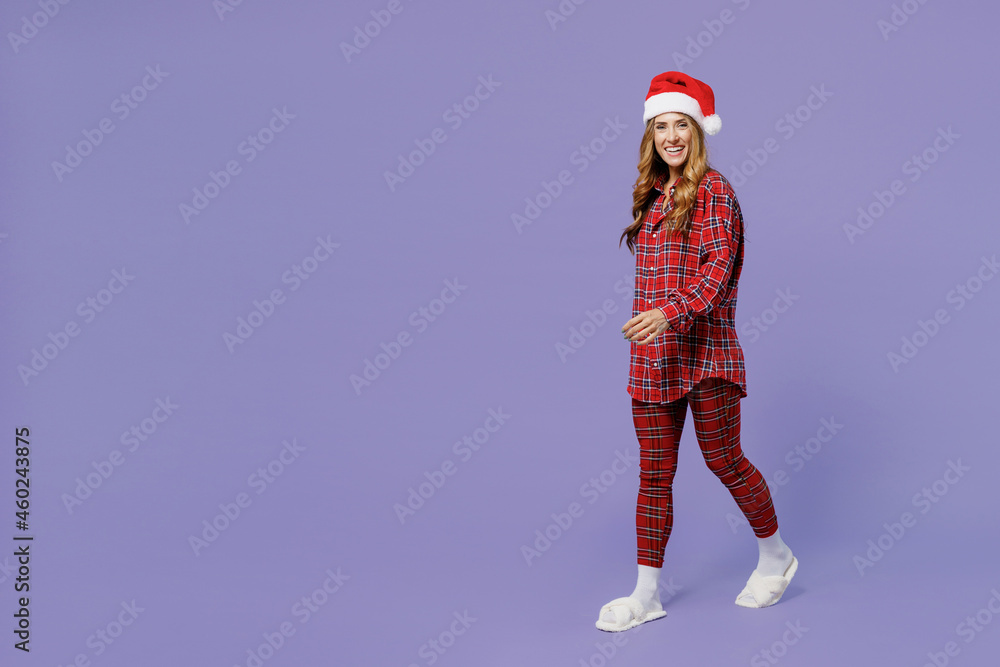 Full size body length fun young Santa woman 30s wears shirt Christmas hat look camera go walk move isolated on plain pastel light violet background studio portrait. Happy New Year celebration concept. Full size body length fun young Santa woman 30s wears shirt Christmas hat look camera go walk move isolated on plain pastel light violet background studio portrait. Happy New Year celebration concept.