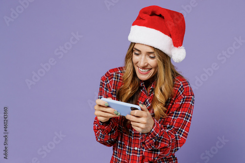 Gambling young Santa woman 30s wear shirt Christmas hat play racing app on mobile cell phone hold gadget smartphone for pc video games isolated on plain pastel light violet background studio portrait