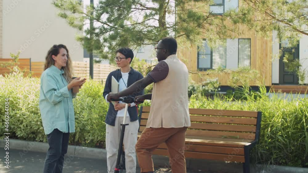Group of young multiethnic colleagues standing on street and having discussion young Caucasian woman explaining something to Asian female colleague and black man Group of young multiethnic colleagues standing on street and having discussion young Caucasian woman explaining something to Asian female colleague and black man