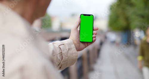 View over shoulder of mature man holding cellphone with blank green screen in city