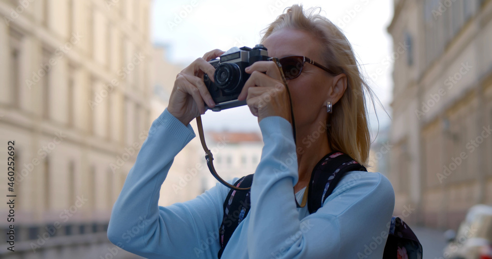 Mature woman in sunglasses taking pictures of old city on retro camera.