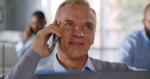 Close up of mature businessman talking on mobile phone sitting at office desk