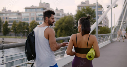 Mixed-race woman and indian man runners walking in sportswear on city bridge