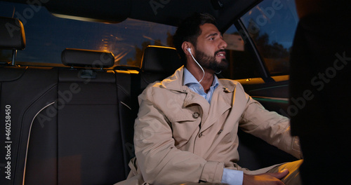 Young businessman listening music through earphones traveling on backseat in car photo