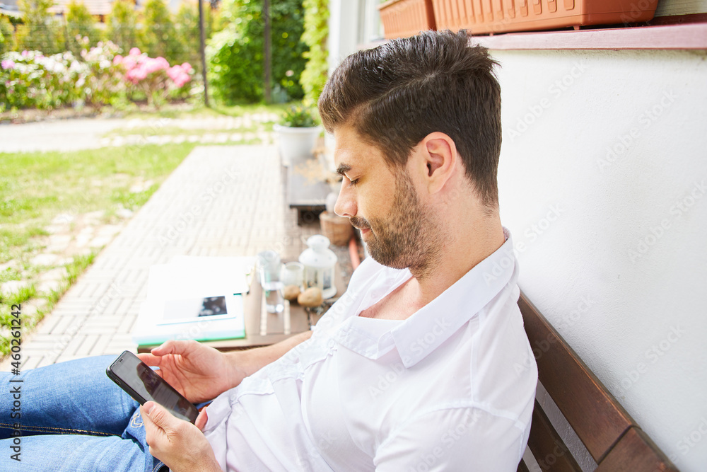 Mann mit Smartphone liest SMS auf der Terrasse Mann mit Smartphone liest SMS auf der Terrasse