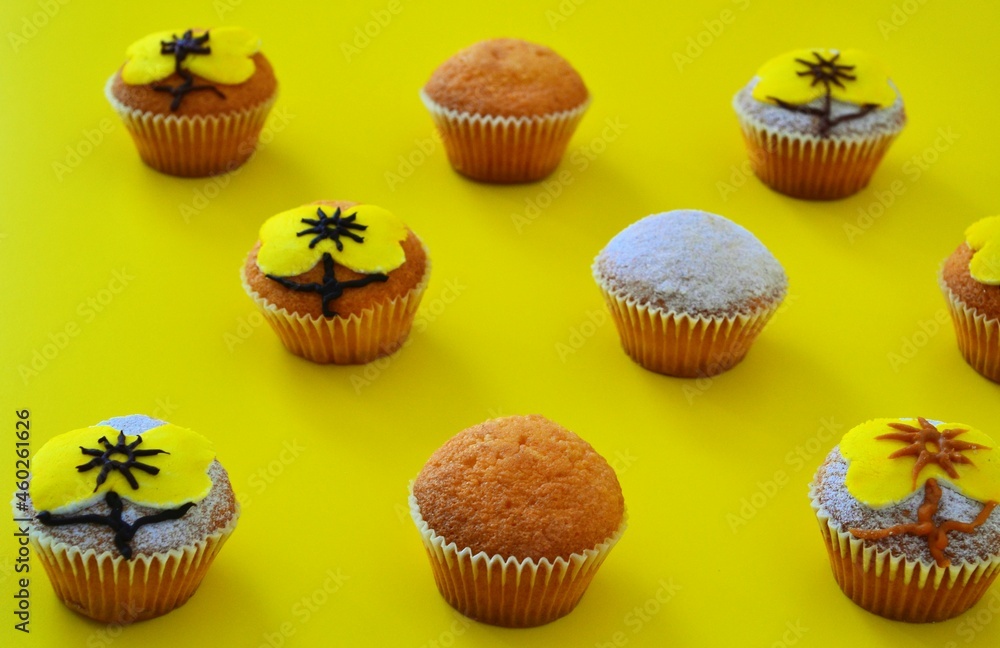 Rows of muffins decorated with powdered sugar and yellow flower shaped icing on a yellow background Rows of muffins decorated with powdered sugar and yellow flower shaped icing on a yellow background