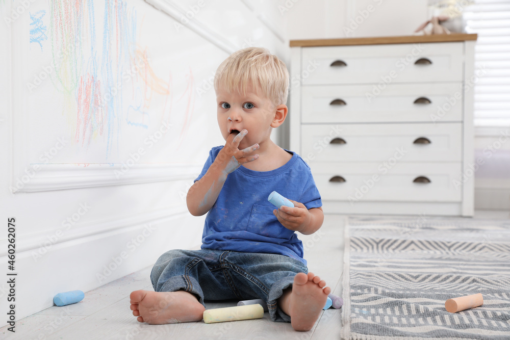 Mischievous little boy near white wall with colorful chalk scribbles at home Mischievous little boy near white wall with colorful chalk scribbles at home