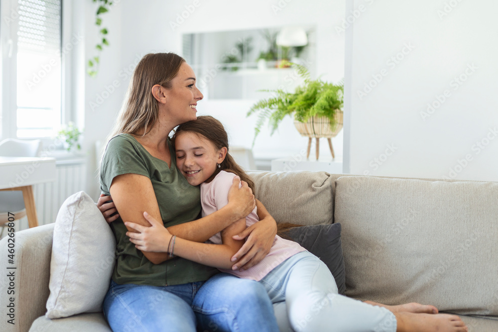 Close up of sweet pretty daughter cuddling with her young mother. Lovely mother embracing her cute daughter on the sofa at home.