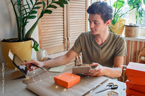 Young millennial worker packing Christmas gift boxes for clients, family small business. New Year celebration, distant work and home office, indoor lifestyle