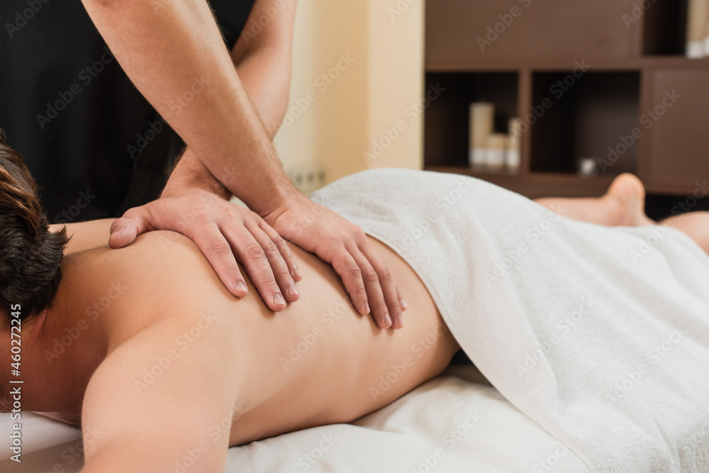 Fototapeta premium Cropped view of masseur doing massage to man in towel in spa center