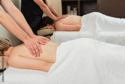 Masseur doing massage to young woman in towel near colleague in spa center
