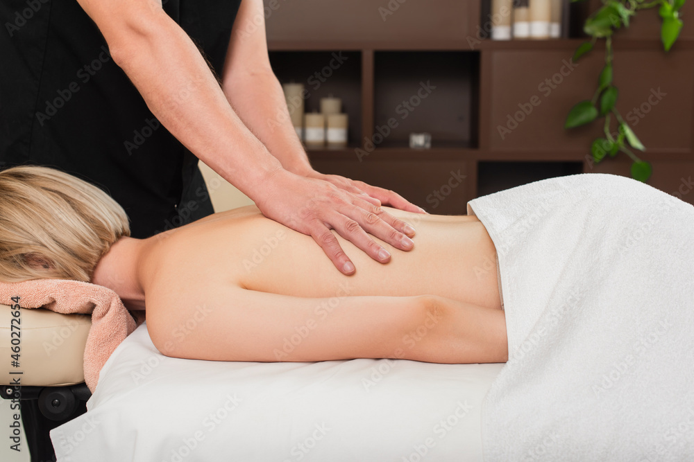 Masseur massaging back of young woman in towel in spa center